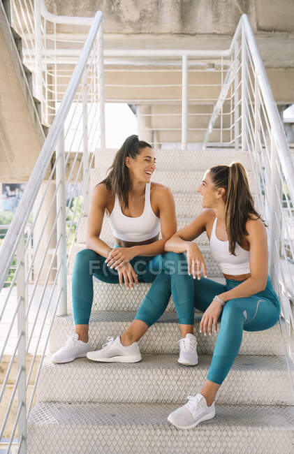 Two happy twin sisters relaxing on stairs after doing sports — Stock Photo