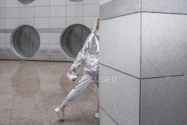 Chica en traje de plata caminando detrás de la pared en la ciudad futurista - foto de stock