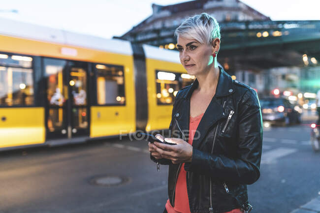 Ritratto di donna bionda in piedi sul ciglio della strada la sera con il cellulare, Berlino, Germania — Foto stock