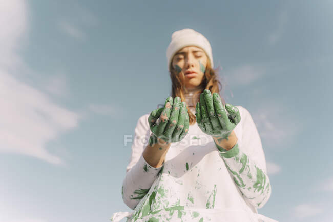 Junge Frau blickt auf ihre grün bemalten Hände herab — Stockfoto
