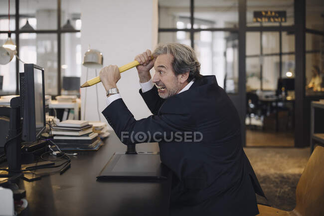 Angry senior uomo d'affari con matita gigante alla scrivania in ufficio — Foto stock