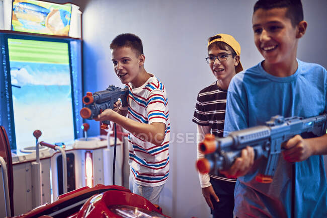 Amigos adolescentes disparando con armas de fuego en un arcade de diversiones - foto de stock