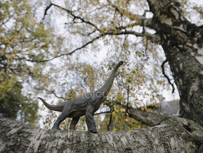 Statuetta di dinosauro su un albero in autunno — Foto stock