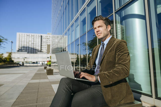 Businessman sitting in urban business district using laptop, Madrid, Spain — Stock Photo