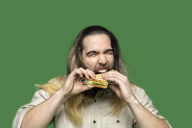 Porträt eines bärtigen Mannes, der vor grünem Hintergrund Sandwich isst — Stockfoto