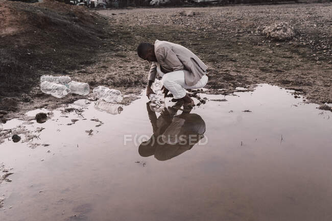 Giovane uomo riempire bottiglia di plastica con acqua in un buco d'acqua — Foto stock