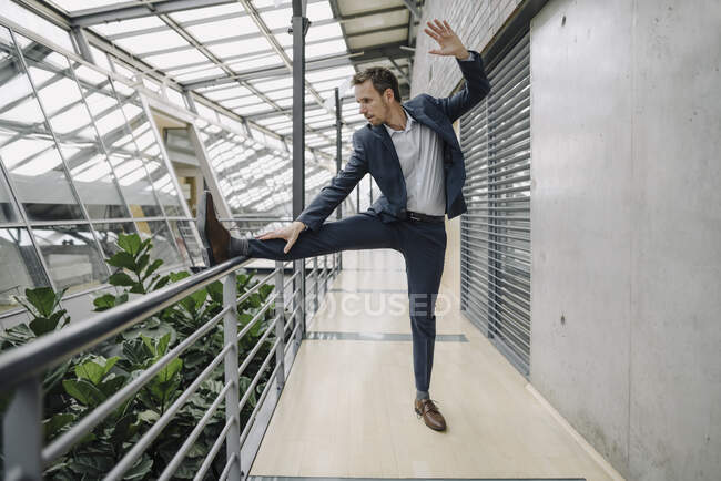 Businessman standing on one leg in modern office — Stock Photo