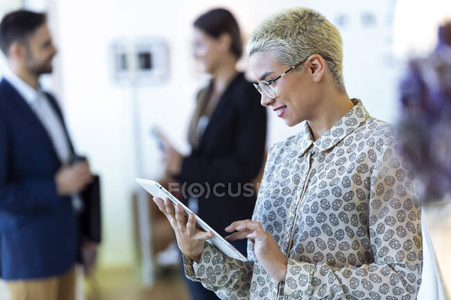 Empresaria que usa tableta en la oficina con colegas en segundo plano - foto de stock
