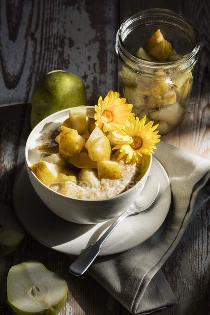 High angle view of porridge with pears and flowers in bowl on wooden table — Stock Photo