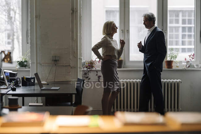 Businessman and businesswoman talking at the window in office — Stock Photo