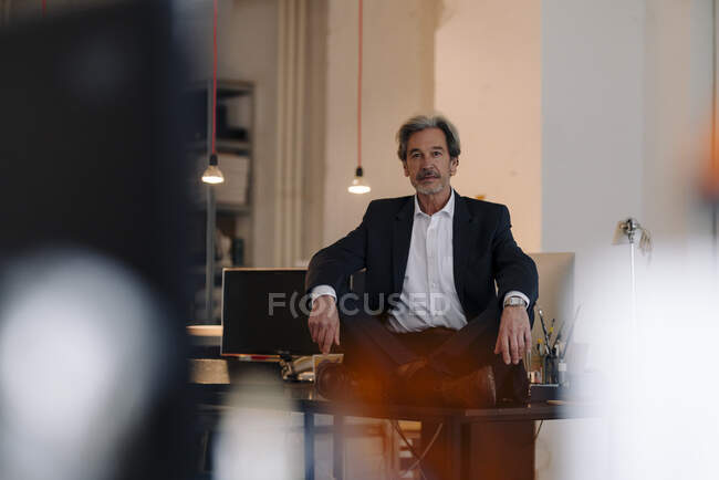 Senior-Geschäftsmann sitzt im Schneidersitz auf Schreibtisch im Büro — Stockfoto