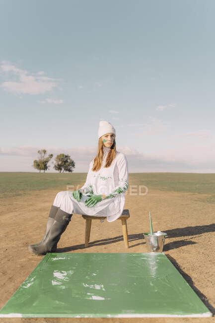 Молода жінка сидить на стільці з зеленим малюнком на сухому полі. — стокове фото