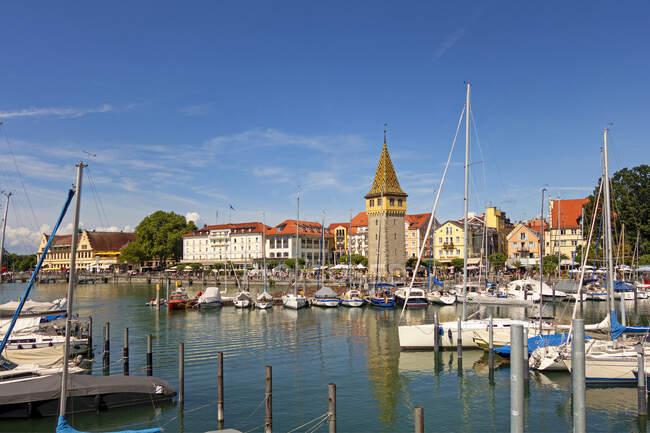 Boats moored at harbor with buildings in background against blue sky, Lindau, Germany — Stock Photo