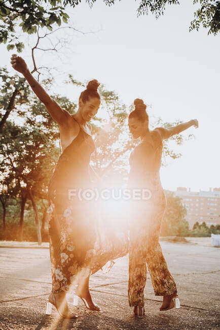 Two cheerful twin sisters dancing outdoors at sunset — Stock Photo