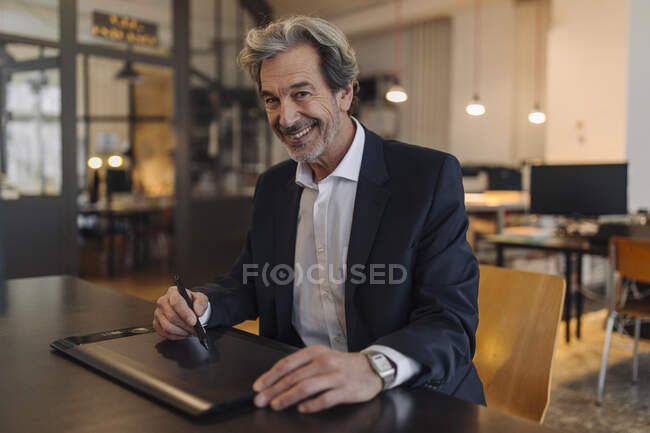 Retrato de un hombre de negocios mayor sonriente usando una tableta gráfica en el escritorio de la oficina - foto de stock