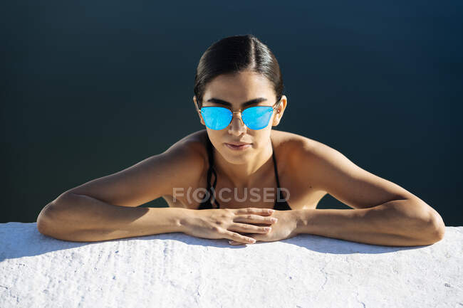 Portrait of young woman wearing sunglasses and bikini leaning on quay wall — Stock Photo