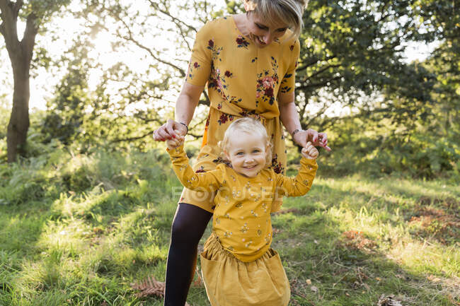 Retrato de una niña rubia mano a mano con su madre en un prado - foto de stock