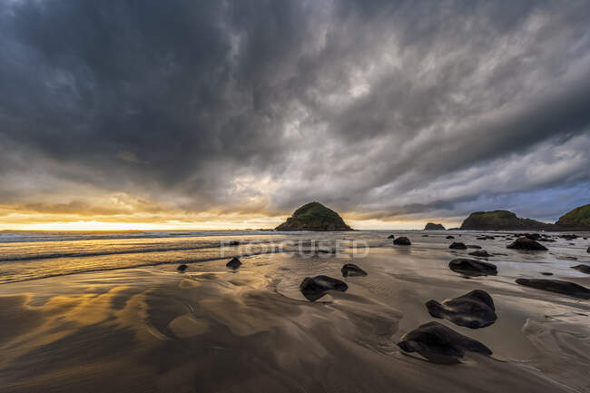 Nuova Zelanda, Tongaporutu, Cielo nuvoloso sulla spiaggia costiera sabbiosa al tramonto con l'isola di Motuotamatea sullo sfondo — Foto stock