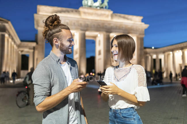 Casal feliz usando smartphones no portão de Brandemburgo na hora azul, Berlim, Alemanha — Fotografia de Stock