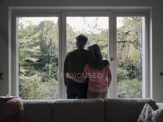 Rückansicht eines Senioren-Paares, das zu Hause aus dem Fenster schaut — Stockfoto