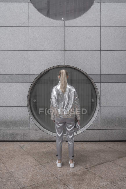 Rear view of girl in silver suit, standing in front of round window — Stock Photo