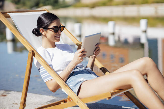 Smiling young woman sitting in a deckchair using tablet — Stock Photo