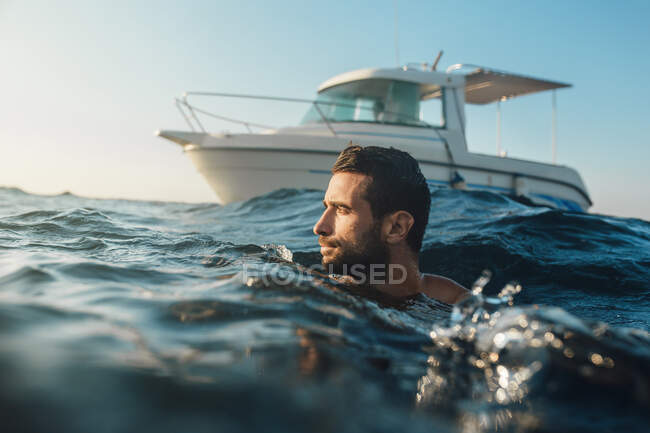 Giovane uomo che nuota nel mare di fronte allo yacht — Foto stock