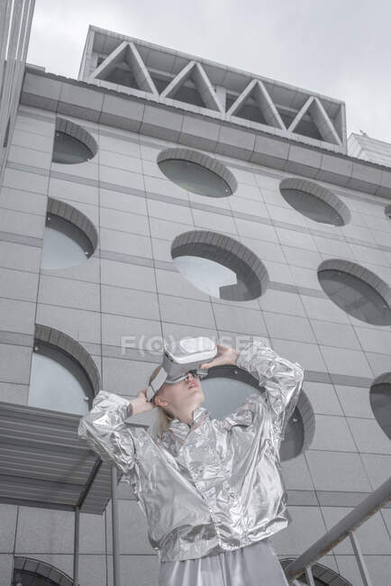 Chica de traje plateado. mirando a través de gafas VR en la ciudad futurista - foto de stock