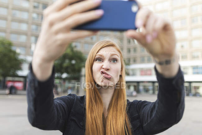 Porträt einer rothaarigen jungen Frau mit schmollendem Mund beim Selfie mit dem Smartphone, Berlin, Deutschland — Stockfoto