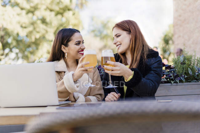 Дві подружки, які чіпляються за пивні склянки на відкритому повітрі в кафе. — стокове фото