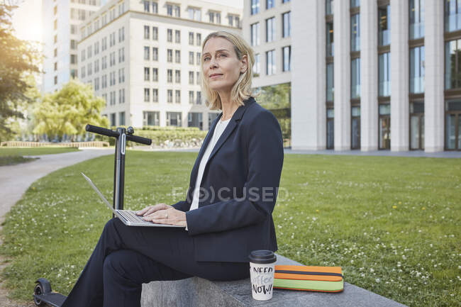 Businesswoman sitting on a wall in the city using laptop — Stock Photo