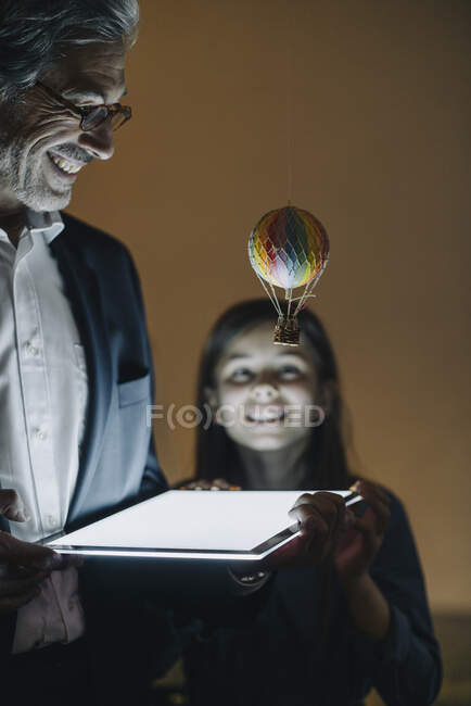 Glückliche Seniorin mit Heißluftballon und leuchtendem Tablet im Büro — Stockfoto