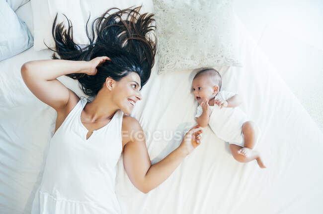 Sorridente madre sdraiata a letto con il suo bambino — Foto stock