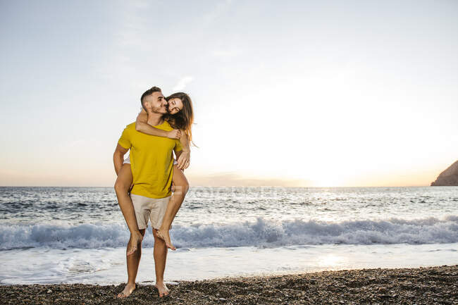 Young couple at the beach at sunset, man carrying laughing woman — Stock Photo