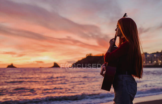 Junge Frau mit Gitarre am Strand bei Sonnenuntergang und Blick auf das Meer, Almunecar, Spanien — Stockfoto