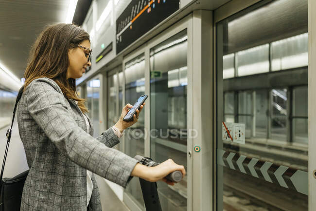 Giovane donna d'affari con e-scooter utilizzando il telefono alla stazione della metropolitana — Foto stock
