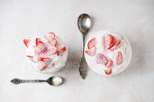 Прямо над рюмкой клубничного мороженого, подаваемого в мисках с ложкой на столе — стоковое фото