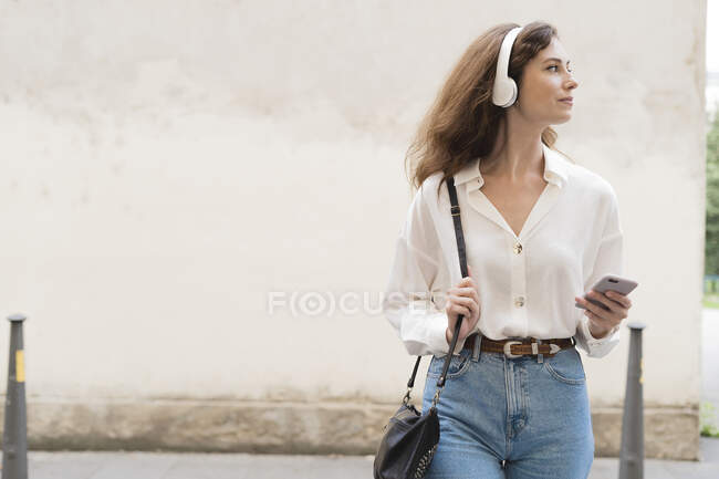 Young woman with smartphone and headphones in the city on the go — Stock Photo