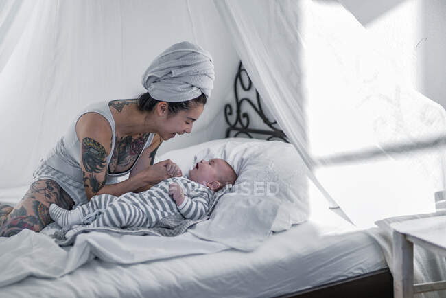 Tattooed young woman with her baby in canopy bed — Stock Photo