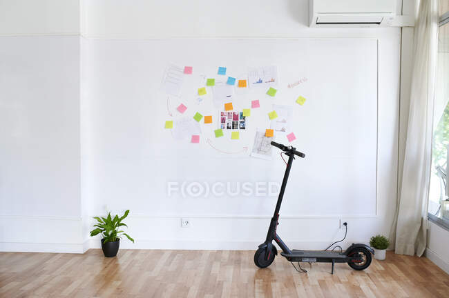 Електричний скутер перед стіною, заповненою липкими нотатками у яскравому сучасному офісі. — стокове фото