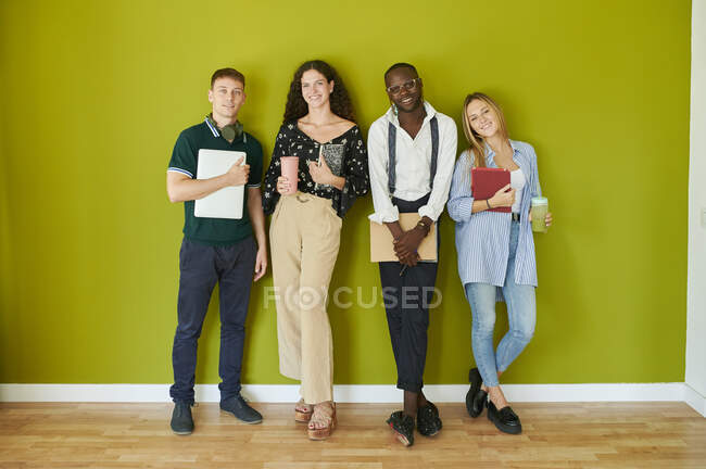 Retrato de colegas casuais sorridentes em pé juntos em frente a uma parede verde em um escritório moderno — Fotografia de Stock