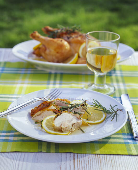 Roasted chicken in lemon sauce and glass of white wine on garden table — Stock Photo