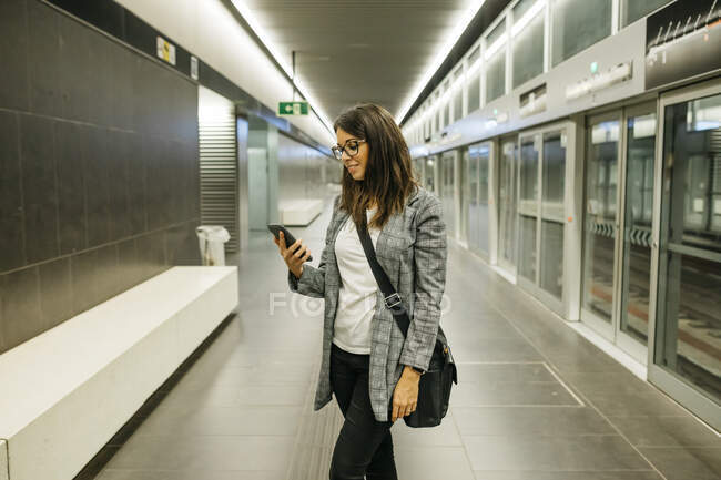 Jeune femme d'affaires utilisant le téléphone à la station de métro, attendant le train — Photo de stock