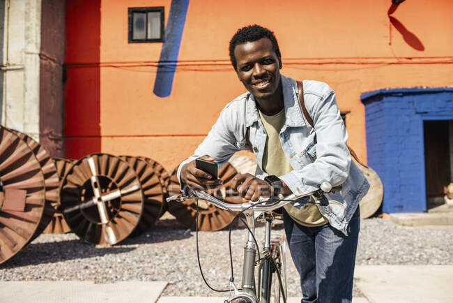 Relajado joven amn conmutar en la ciudad con la bicicleta hos, utilizando el teléfono inteligente - foto de stock
