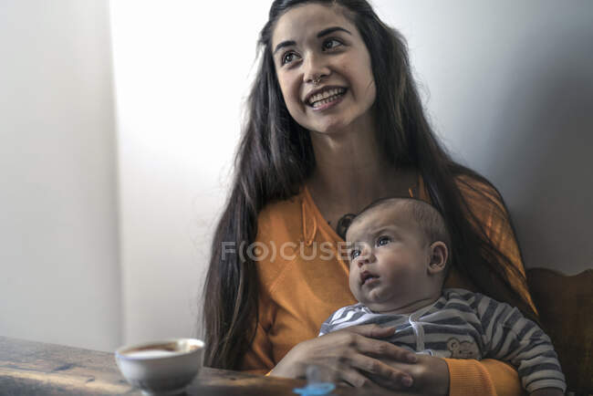 Mère heureuse avec bébé assis à la table en bois à la maison — Photo de stock