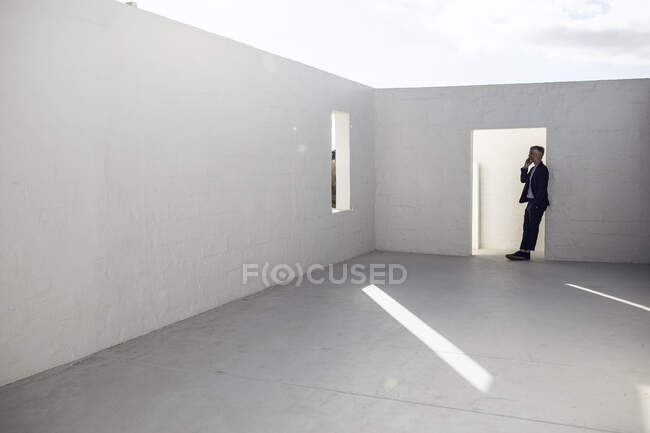 Бизнесмен, прислонившись к дверной раме пустого пространства, разговаривает по телефону — стоковое фото