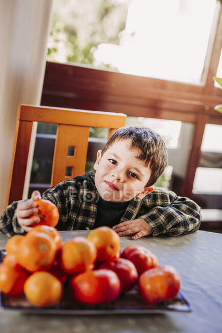 Boy sitting on the tabel and taking a clementine — Stock Photo