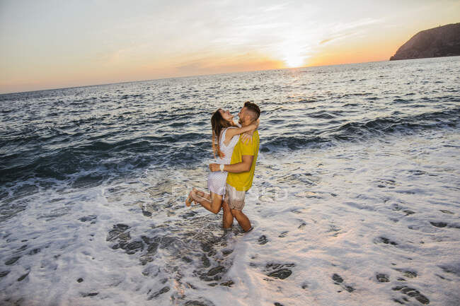 Jeune couple à la plage pendant le coucher du soleil — Photo de stock