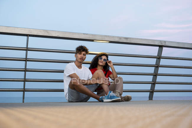 Молода пара сидить на мосту біля моря. — стокове фото