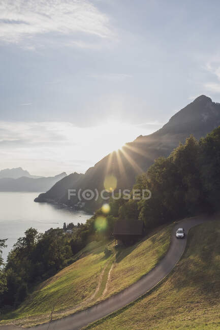 Suiza, Gersau, Schwyz, Coche que conduce a lo largo de la carretera sinuosa al atardecer con el lago de Lucerna en el fondo - foto de stock